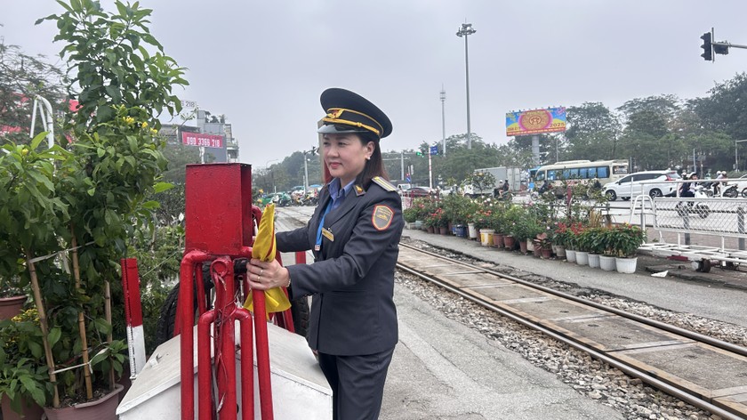 Khi tiếng chu&ocirc;ng th&ocirc;ng b&aacute;o vang l&ecirc;n c&ugrave;ng t&iacute;n hiệu đ&egrave;n b&aacute;o, chị Nh&agrave;n v&agrave; c&aacute;c đồng nghiệp đội mũ k&ecirc;pi, tay cầm cờ hiệu di chuyển ra đường ray k&eacute;o thanh chắn, đảm bảo an to&agrave;n khi t&agrave;u chạy qua. Ảnh: Ngọc Nga