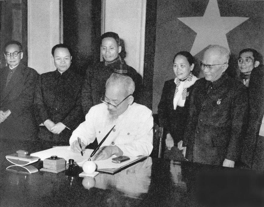 Chủ tịch Hồ Ch&iacute; Minh k&yacute; sắc lệnh c&ocirc;ng bố Hiến ph&aacute;p năm 1959. Bộ trưởng Bộ Tư ph&aacute;p Vũ Đ&igrave;nh H&ograve;e đứng ngo&agrave;i c&ugrave;ng, b&ecirc;n tr&aacute;i. Ảnh tư liệu