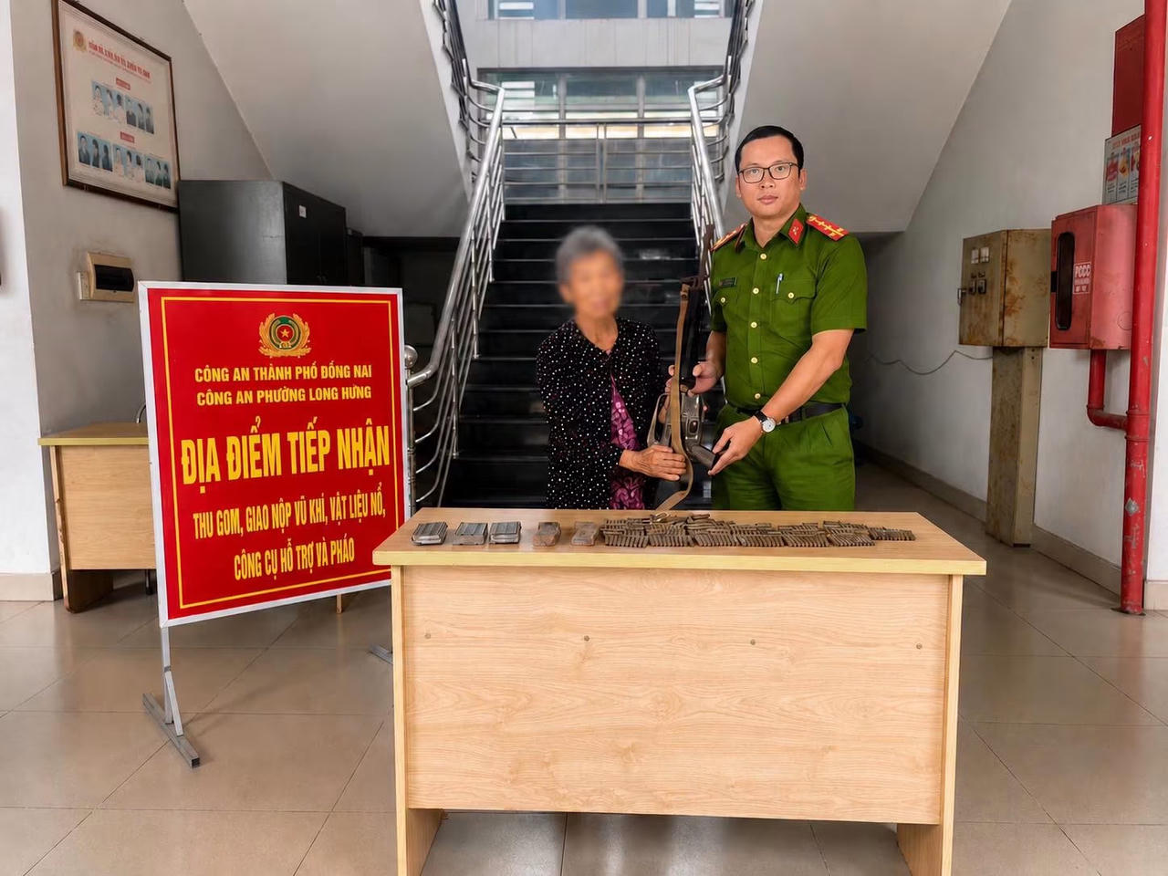B&agrave; L. b&agrave;n giao số vũ kh&iacute; cho C&ocirc;ng an phường Long Hưng.