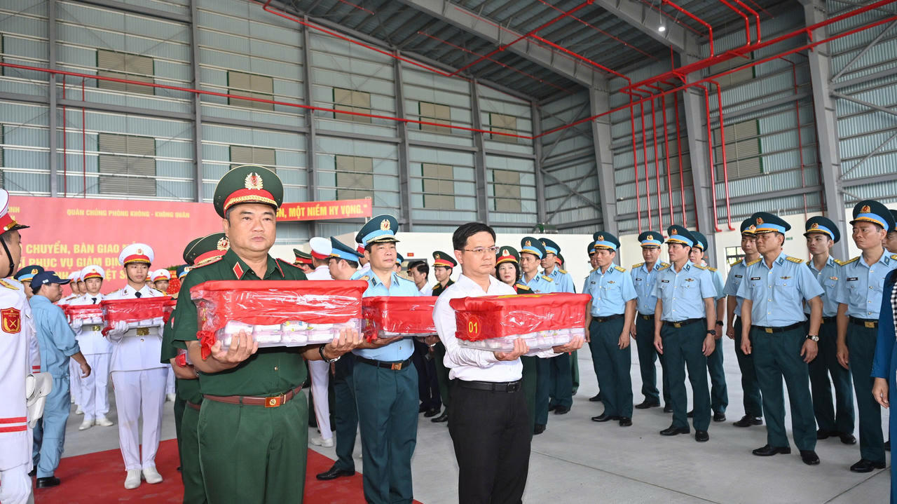 Trung tướng L&ecirc; Xu&acirc;n Thế, Tư lệnh Qu&acirc;n khu 7 (b&igrave;a tr&aacute;i) v&agrave; Ủy vi&ecirc;n dự khuyết Trung ương Đảng, Ph&oacute; chủ tịch UBND TP.HCM, Trưởng Ban Chỉ đạo 515 th&agrave;nh phố Nguyễn Mạnh Cường (sơ mi trắng) đưa th&ugrave;ng chứa mẫu sinh phẩm h&agrave;i cốt liệt sĩ l&ecirc;n m&aacute;y bay. (Ảnh: Xu&acirc;n Sang)