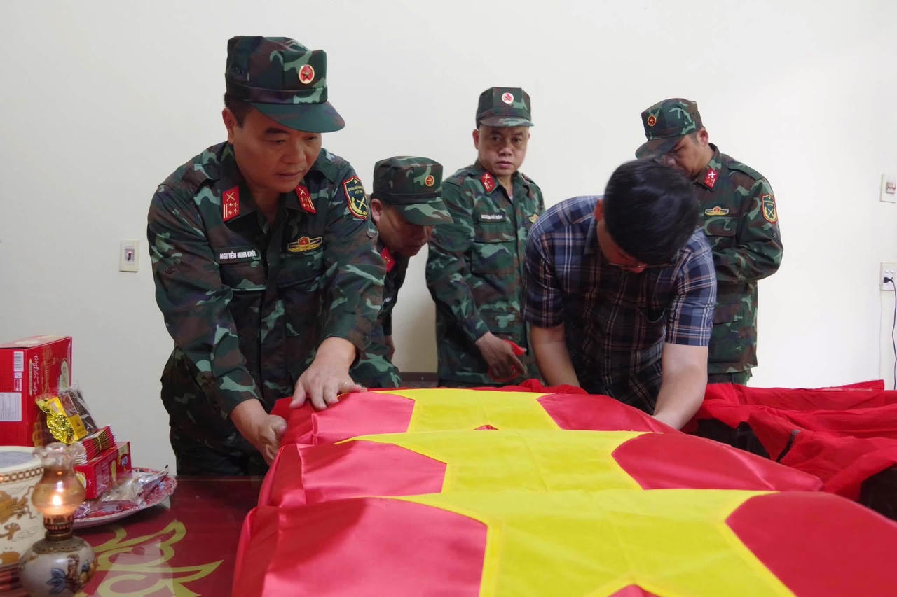 Đại t&aacute; Nguyễn Minh Kh&ocirc;i, Ph&oacute; Ch&iacute;nh ủy BCH Qu&acirc;n sự tỉnh Tuy&ecirc;n Quang, &ocirc;ng L&yacute; Nam Thuỷ, B&iacute; thư Đảng uỷ x&atilde; Minh T&acirc;n thực hiện nghi lễ đưa h&agrave;i cốt liệt sĩ v&agrave;o &aacute;o quan v&agrave; phủ Cờ Tổ quốc. (Ảnh: BCHQS tỉnh Tuy&ecirc;n Quang)